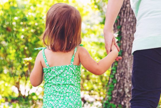 Toddler girl holding hands with her mother who contacted a child support attorney rochester outside on a summer day